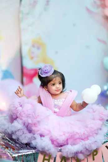 Smiling baby girl in a lilac tutu on a pastel birthday set