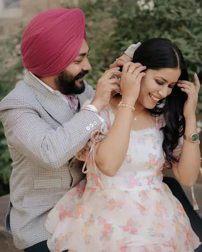 Groom in a pink turban tucking his bride's hair behind her ear in a garden